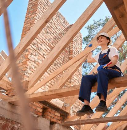 Woman roofer sitting on roof beam and enjoying done roofing works